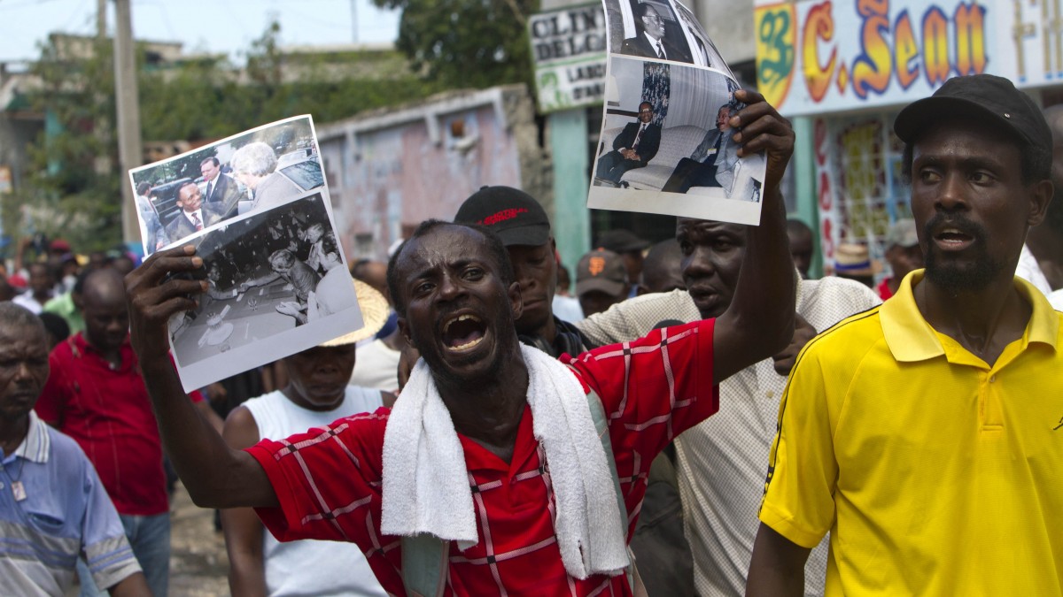 A demonstrator holds up images of former Haiti's President Jean Bertrand Aristide during a protest in Port-au-Prince, Haiti, Sunday, Oct. 14, 2012. Hundreds of people protested in Haiti's capital over what they say is a higher cost of living. The demonstrators marched through the cinderblock shanties of downtown Port-au-Prince as they criticized the policies of President Michel Martelly. (AP Photo/Dieu Nalio Chery)