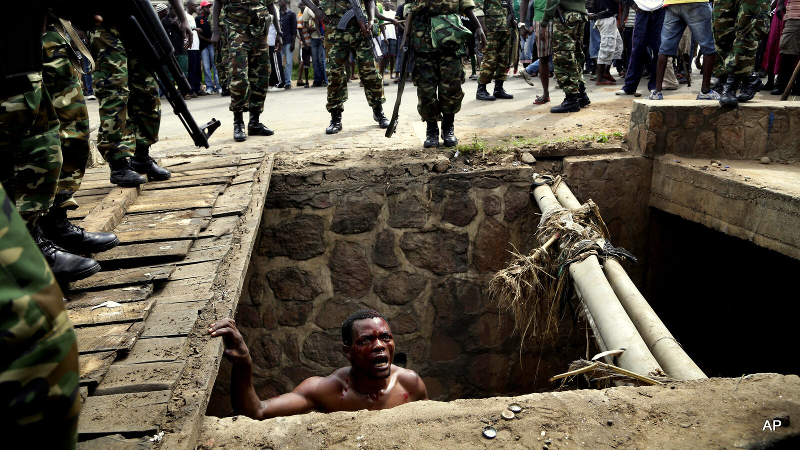 Jean Claude Niyonzima, a suspected member of the ruling party's Imbonerakure youth militia, pleads with soldiers to protect him from a mob of demonstrators after he emerged from hiding in a sewer in the Cibitoke district of Bujumbura, Burundi, Thursday May 7, 2015. Niyonzima fled from his house into a sewer under a hail of stones thrown by a mob protesting against President Pierre Nkurunziza's decision to seek a third term in office. At least one protestor has died in clashes with the widely feared Imbonerakure militias and police, sending scores to the streets seeking revenge. Jean Claude Niyonzima managed to flee from his house under a hail of stones into a covered sewer, where he remained till the army fired shots into the air to disperse the crowd.