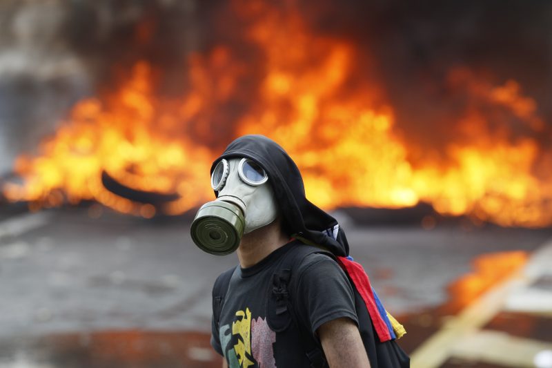 An anti-government protester stands in front of burning barricade on a highway in Caracas, Venezuela, Monday, April 24, 2017. Thousands of protesters shut down the capital city' class=